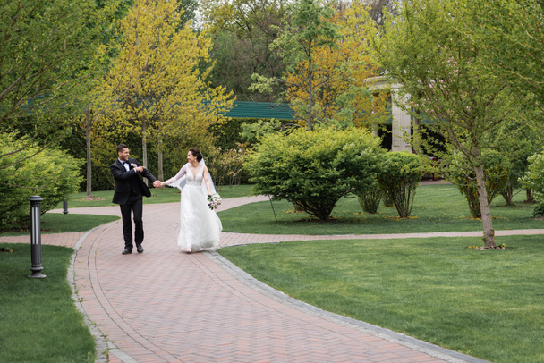 Веселый жених указывает пальцем на невесту во время прогулки в парке  - Фото, изображение
