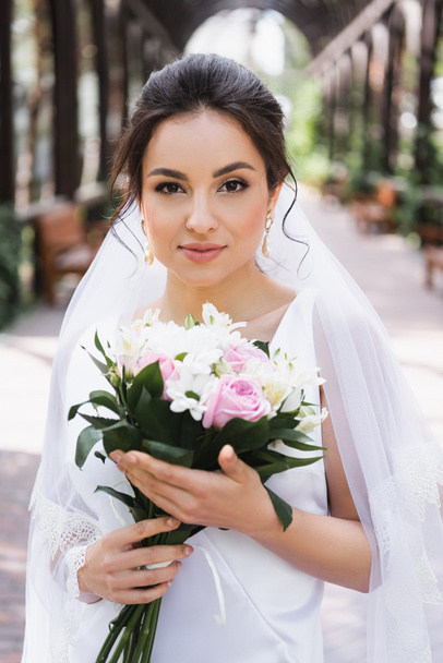 Bride with bouquet looking at camera outdoors  - Fotografie, Obrázek