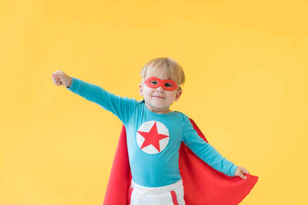 Superhero child against yellow paper background. Super hero kid wearing red mask and cape. Childhood dream and imagination concept - Fotoğraf, Görsel