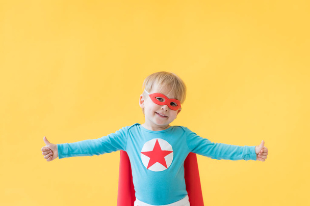 Superhero child against yellow paper background. Super hero kid wearing red mask and cape. Childhood dream and imagination concept - Foto, afbeelding