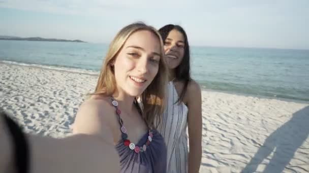 Dwie dziewczyny z gen najlepszych przyjaciół w technologii wideokonferencji pov za pomocą smartfona do rozmowy wideo na tropikalnej plaży z białym piaskiem o zachodzie lub świcie. Nowoczesna technologia do utrzymywania więzi przyjaźni - Materiał filmowy, wideo