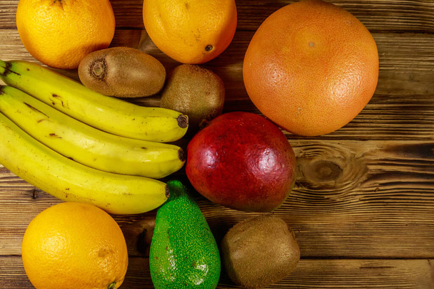 Асортимент тропічних фруктів на дерев'яному столі. Натюрморт з бананами, манго, апельсинами, авокадо, грейпфрутами та ківі. Вид зверху
 - Фото, зображення