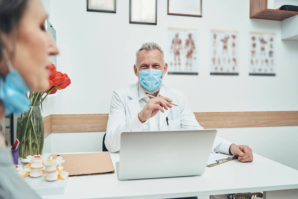 Arzt mit Gesichtsmaske schaut eine grauhaarige Dame an - Foto, Bild