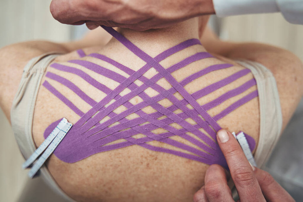 Physiotherapeut stabilisiert den Trapezmuskel mit dem elastischen Therapieband - Foto, Bild