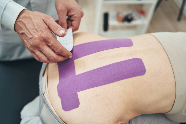 Experienced physiatrist using kinesiology taping method for low back pain - Photo, Image