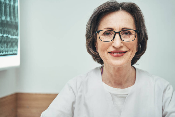 Freudige Physiotherapeutin mit Brille sitzt in ihrem privaten Büro - Foto, Bild