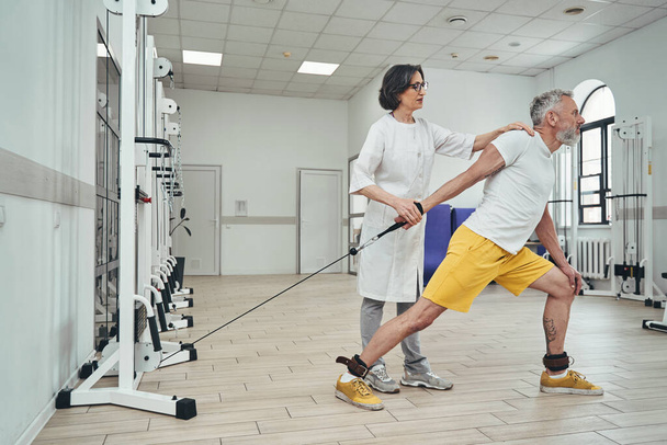Atleta che esegue un esercizio di forza supervisionato da un fisioterapista - Foto, immagini