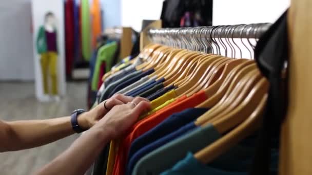 服屋の女の子、女性は店でTシャツを選ぶ、販売、新しいコレクション、女性は男のための贈り物を買う - 映像、動画