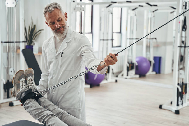 Soustředěný kineziolog rehabilituje svého klienta pomocí tělocvičny - Fotografie, Obrázek