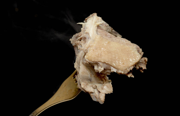 Kawałek gotowanego mięsa z kurczaka na widelcu, dym parowy, czarne tło. - Zdjęcie, obraz