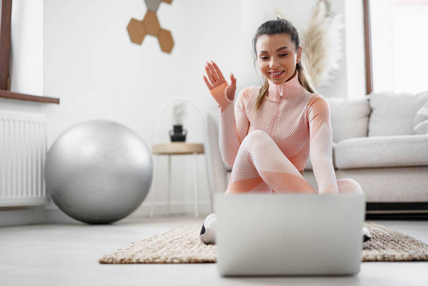 Young woman in sportswear using laptop to watch workout video tutorials at home - Photo, image