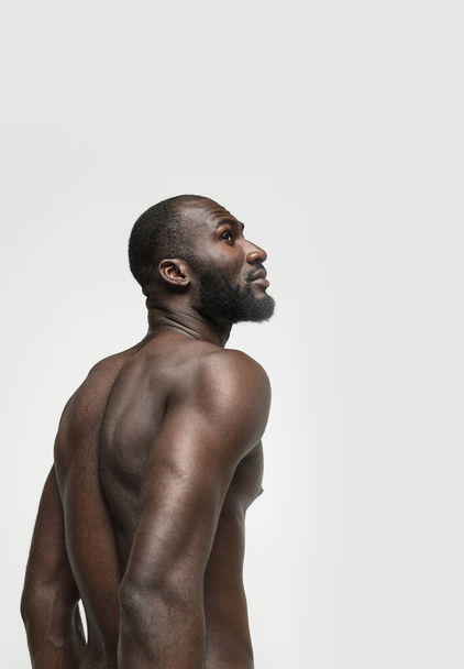 Портрет молодого красивого мускулистого африканца, позирующего на белом фоне. Вид сзади - Фото, изображение