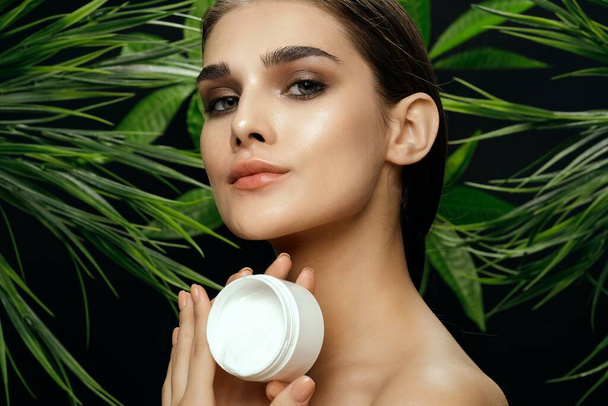 woman with a jar of cream near green leaves of palm bushes Exotic jungle clean skin - Foto, Bild