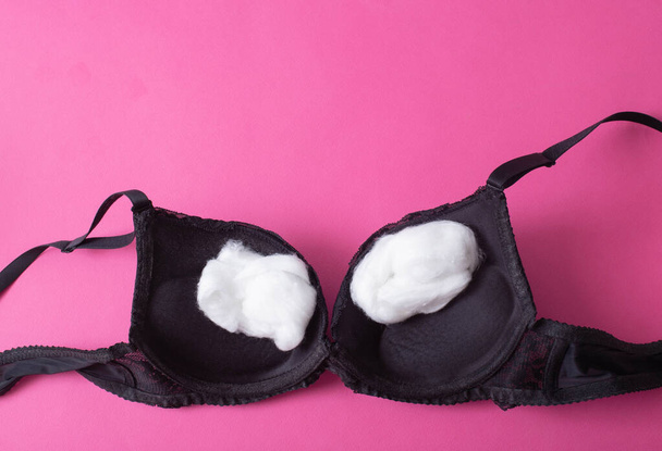 black female bra with cotton wool inside on a pink background. The concept of augmentation of the female breast with plastic surgery - Fotoğraf, Görsel