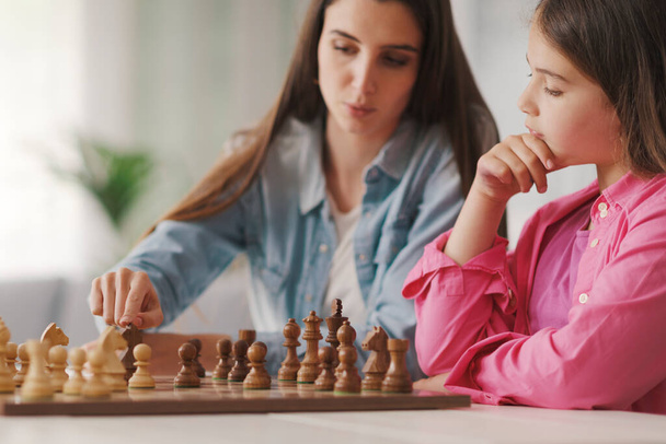 Young mother teaching chess to her kids they are sitting together and playing - Photo, image