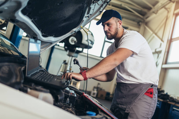 Mécanicien automobile professionnel travaillant dans le service de réparation automobile à l'aide d'un ordinateur portable. - Photo, image