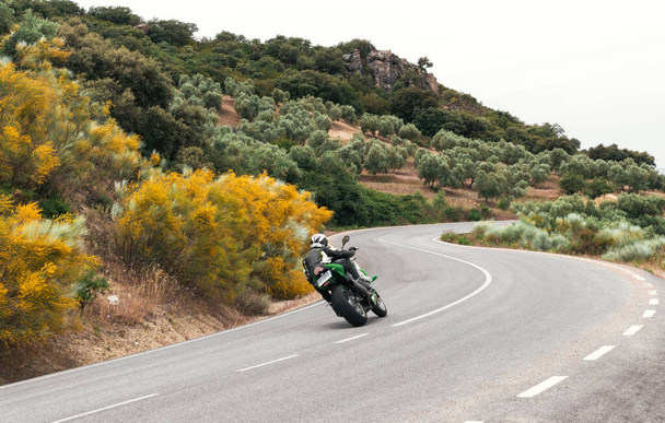 rowerzysta jazda na zielonym motocyklu biorąc zakręt na drodze górskiej.  - Zdjęcie, obraz