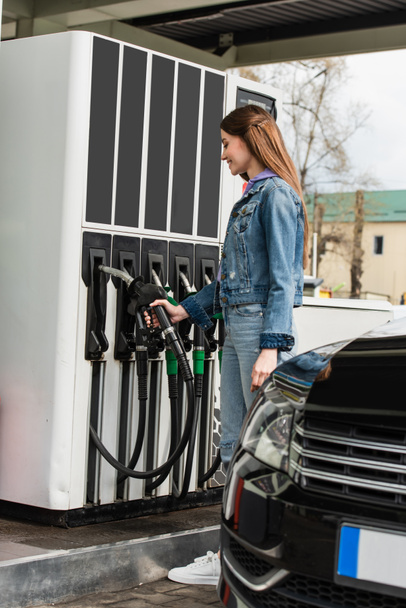 Nuori nainen, jolla on bensiini pistooli lähellä autoa huoltoasemalla - Valokuva, kuva