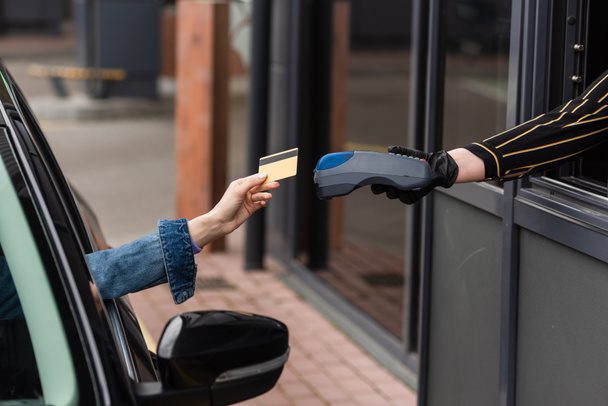 Ödeme terminali olan lateks eldivenli bir kadının yanında kredi kartı olan sürücünün kırpılmış görüntüsü - Fotoğraf, Görsel