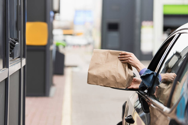 partial view of woman in car holding paper bag with takeaway food - Foto, afbeelding