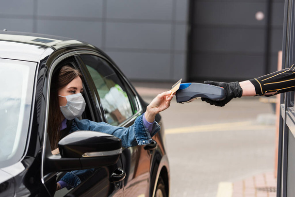 Frau in Schutzmaske zahlt im Auto mit Kreditkarte am Terminal - Foto, Bild