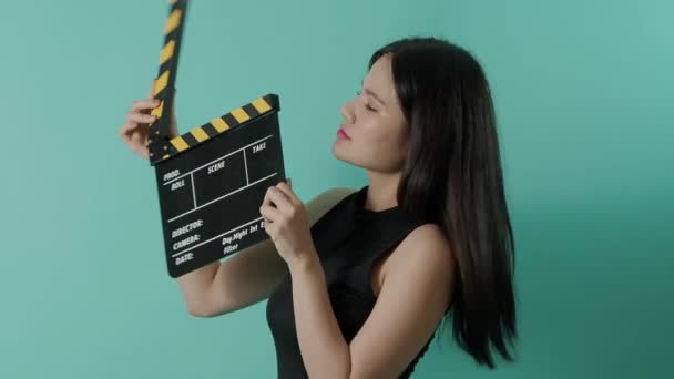 Filmschiefer und kleine sexy süße asiatische Mädchen. Frau hält und klatscht Filmklappbrett oder Filmtafel mit grünem Leinwandhintergrund. Kamera zoomt ein und aus, um ihr Lächeln zu zeigen. Videoproduktion. - Filmmaterial, Video