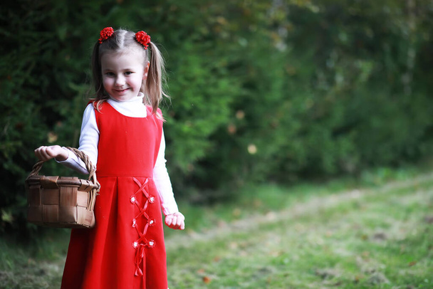 Una bambina con un cappello rosso e dei vestiti sta camminando nel parco. Cosplay per l'eroe fiabesco "Cappuccetto Rosso" - Foto, immagini
