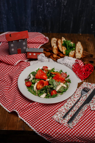 tomatoes, peppers and greens on a white plate and slices of bread with herbs on a wooden tray - Photo, image