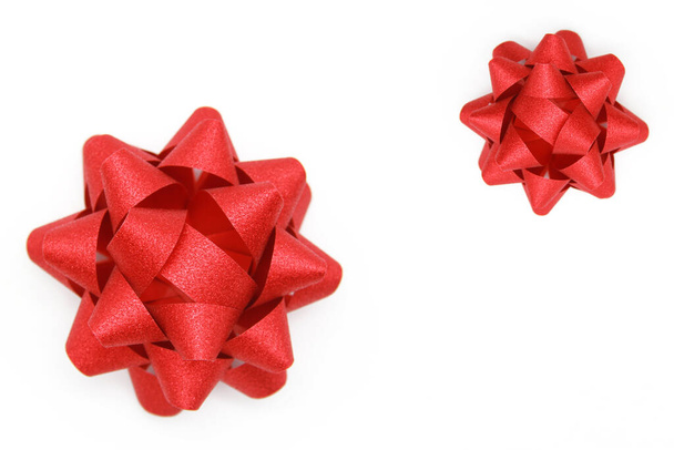 Two beautiful, red, shiny holiday bows(large and small), an addition to the gift box on a white background. Greeting card design concept, gift box.Top view.Flatly.Copyspace. - 写真・画像