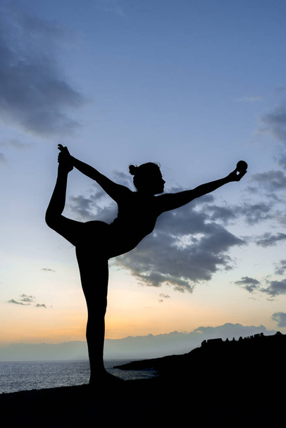 A vertical shot of the silhouette of a young woman doing a yoga pose and holding out an apple in one hand - Photo, Image
