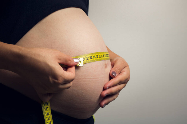 Egy nő hasa, aki terhes egy fiúval, aki sárga mérőszalaggal méri a baba fejlődését és fejlődését elemző kerületet. Említés az egészségről, az étrendről és a jólétről. - Fotó, kép
