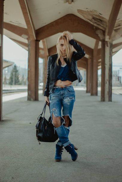 A vertical shot of a sexy Bosnian blonde woman with tall blue boots under an old building - 写真・画像