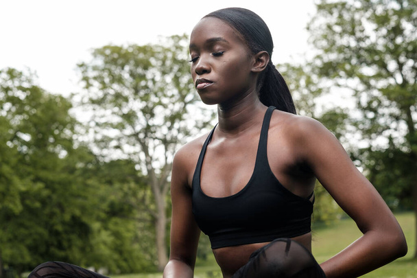 Jonge zwarte vrouw doet meditatie en yoga in een park. Ze draagt zwarte sportkleding.. - Foto, afbeelding