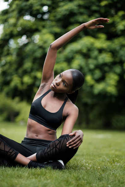 Młoda czarna kobieta uprawiająca medytację i jogę w parku. Ma na sobie czarny strój sportowy.. - Zdjęcie, obraz