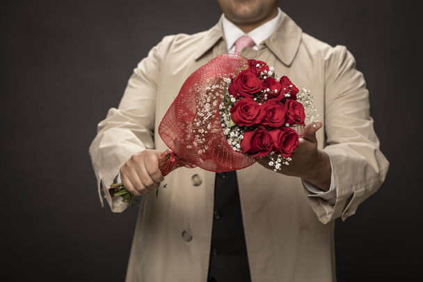 Young man in raincoat in love with bouquet of red roses for his girlfriend. Valentine's Day. - Photo, Image