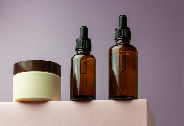Composition with bottles of essential oils and cream jar packaging on a pink background. Natural SPA cosmetic products background. Flat lay, copy space. - 写真・画像