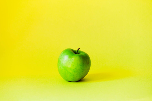 明るい黄色の背景の真ん中に大きな緑色のリンゴが1つ立っています。. - 写真・画像