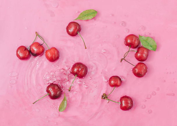 Fresh cherry fruits and leaves in pink water. Creative food background. Minimal summer scene. - Foto, immagini