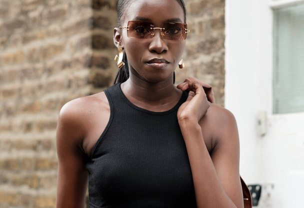 Портрет чорної жінки в моді, позуючи з сонцезахисними окулярами. Вона дивиться на камеру
. - Фото, зображення