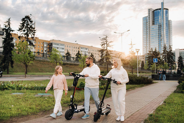 A family in white clothes walks around the city with electric scooters at sunset.Outdoor activities - 写真・画像