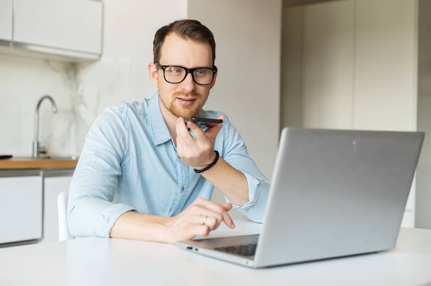 Smart young man sits at the kitchen desk and works remotely from home - Photo, Image