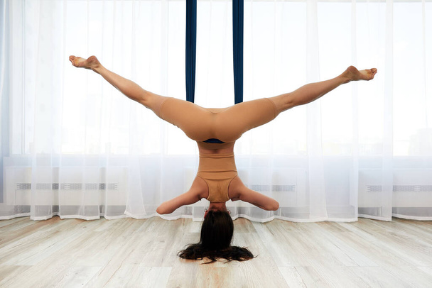 Uitzicht van achteren, een jonge vrouw tijdens de training in een iro hangmat, doen anti-zwaartekracht yoga ondersteboven doen anti-zwaartekracht yoga in een hangmat in de studio, lichte achtergrond, kopieer ruimte - Foto, afbeelding