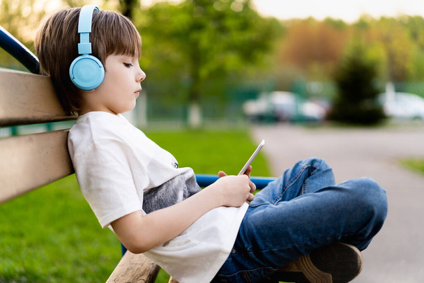 boy on the street sits on a bench with headphones and with a phone - Photo, Image
