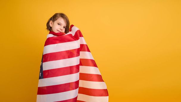 Happy child, cute girl with American flag on yellow studio background. USA celebrate July 4th, independence Day. - Foto, Imagen