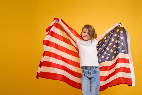 Щаслива дитина, мила дівчина з американським прапором на жовтому тлі студії. США святкують 4 липня День незалежності. - Фото, зображення
