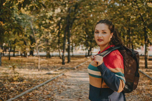 Young plus size traveler girl with backpack traveling along Europe autumn city, fall park. Solo travel, freedom and active lifestyle concept - Foto, Bild