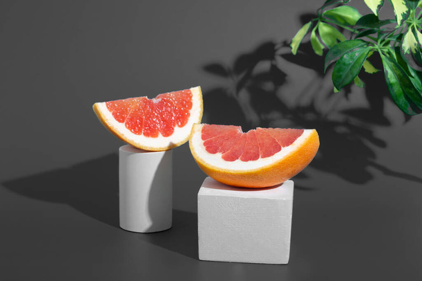Grapefruit slices, fresh healthy grapefruit on the podium with hard shadows. Minimal food creative concept on dark gray background. Citrus still life. - Foto, imagen