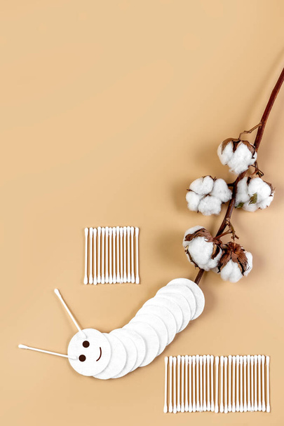 A branch of cotton, cotton wool and cotton buds on a beige background. Natural cotton products. Concept. Care products. Place for your text. - Photo, Image