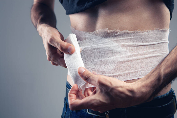 man bandages his stomach on a gray background - Фото, зображення