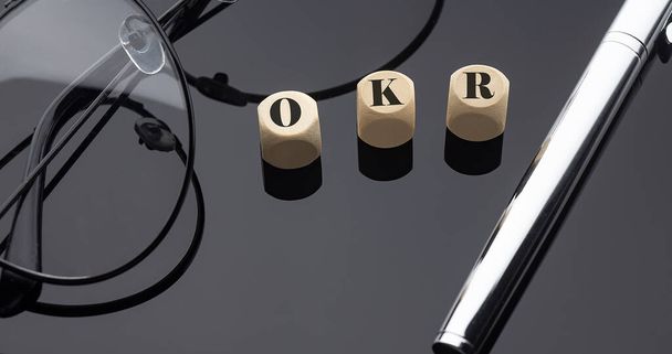 OKR kavramı, tahta bloklardaki kelimeler siyah zemin üzerinde kalem ve gözlüklerle. - Fotoğraf, Görsel